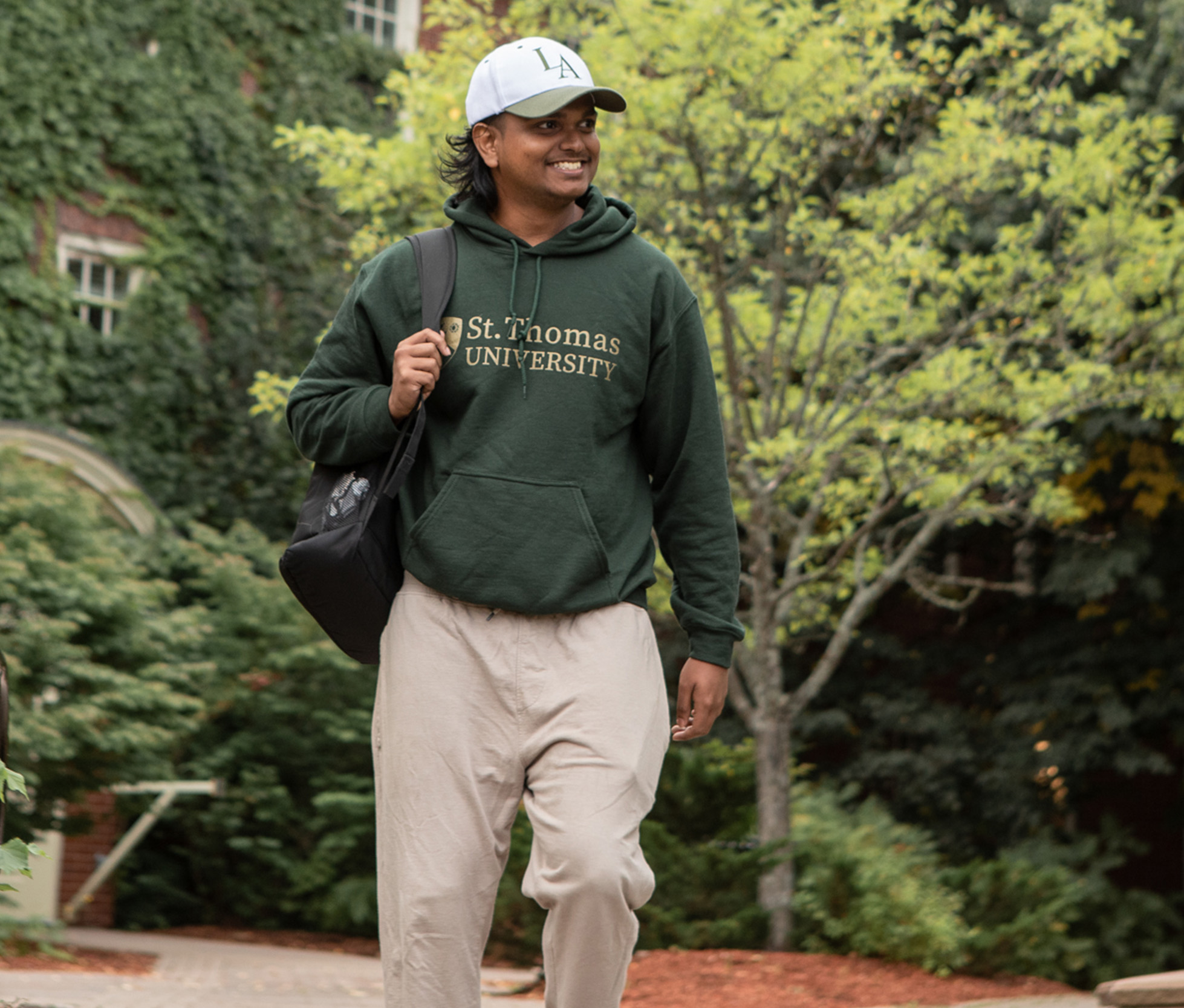 A male student wearing a green St. Thomas University hoodie walks through campus