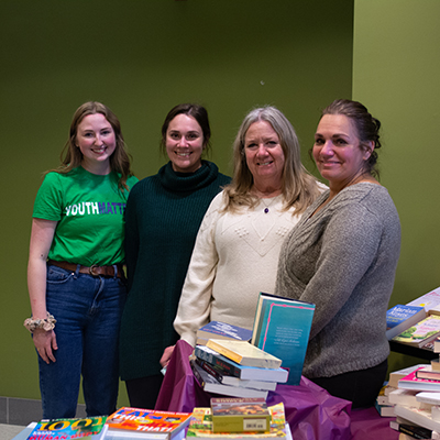 Criminology Professor and three collaborators/supporters smiling and standing in classroom next to books to donate for social justice book drive