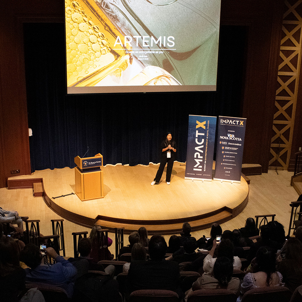 A female student stands on a stage speaking to the audience
