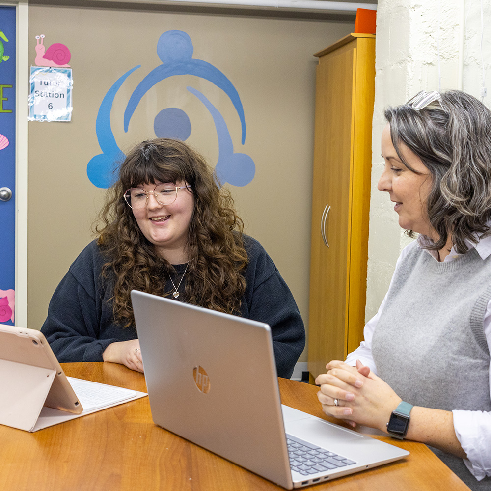 A female student sits at a table with her laptop beside her internship supervisor