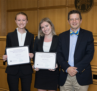 Two female students holding awards next to a judge at a Moot Court competition