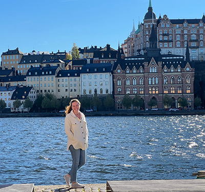 A student stands along the riverfront in Stockholm, Sweden with scenic buildings in the background