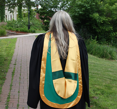 A student wearing a graduation robe and a green and gold MSW hood