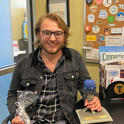 STUdent Noah Deas sits holding his award in the Experiential Learning Office
