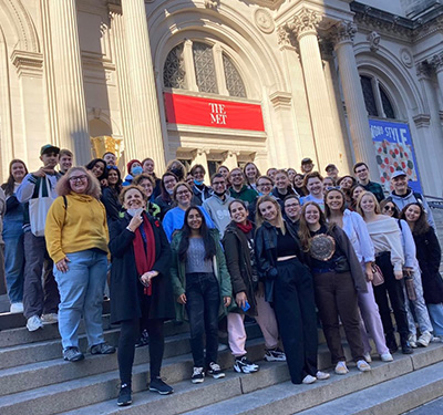 A group of students and professors stand on the steps of the Metropolitan Museum of Art in New York City