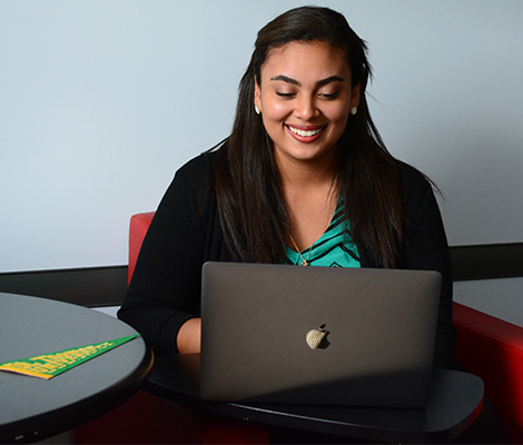 A student sitting in a conference room working on a laptop with a STU pennant on the table