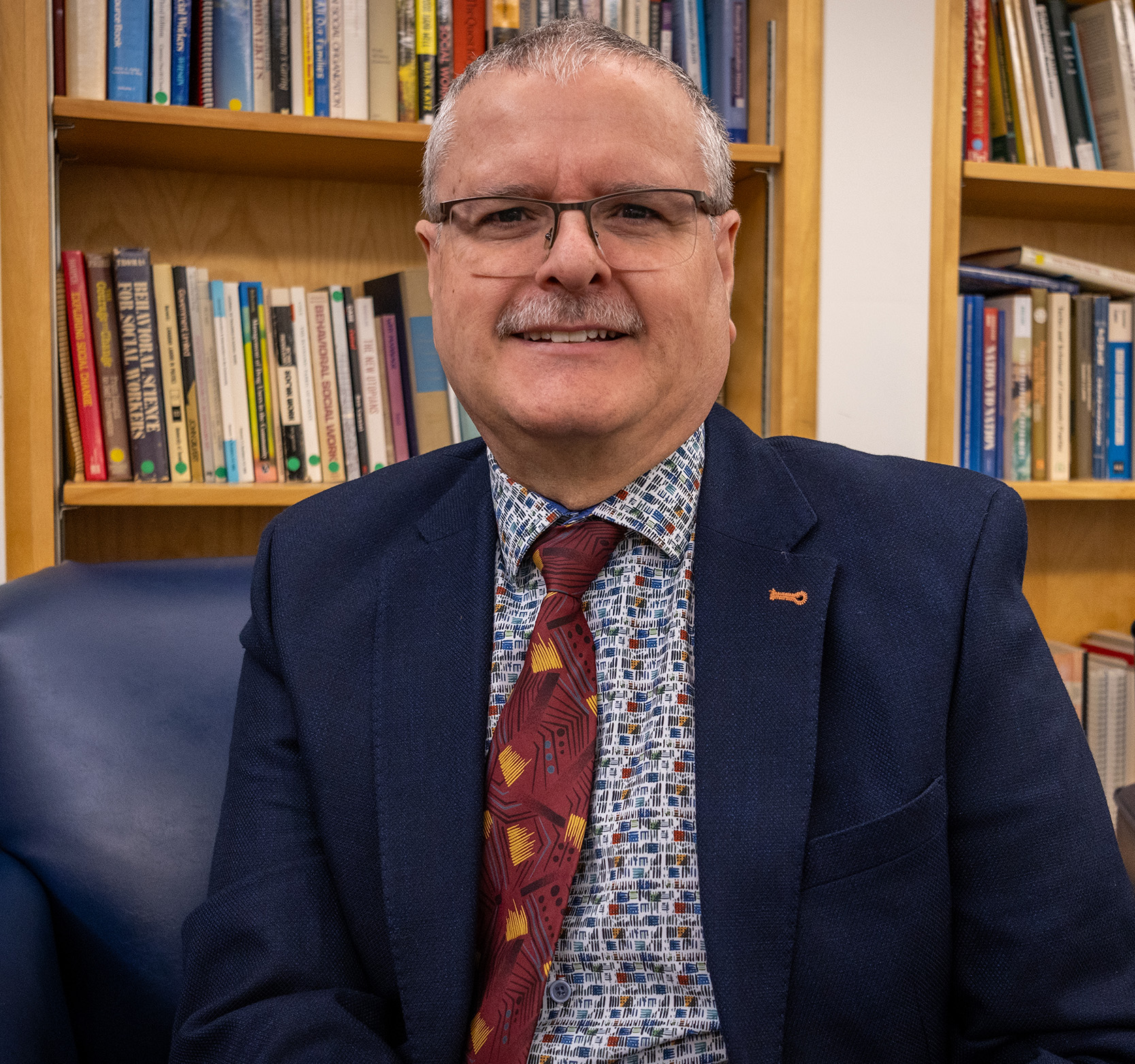 Professor Leo-James Levesque, sitting in front of a book shelf in the Brian Mulroney Hall Rotunda