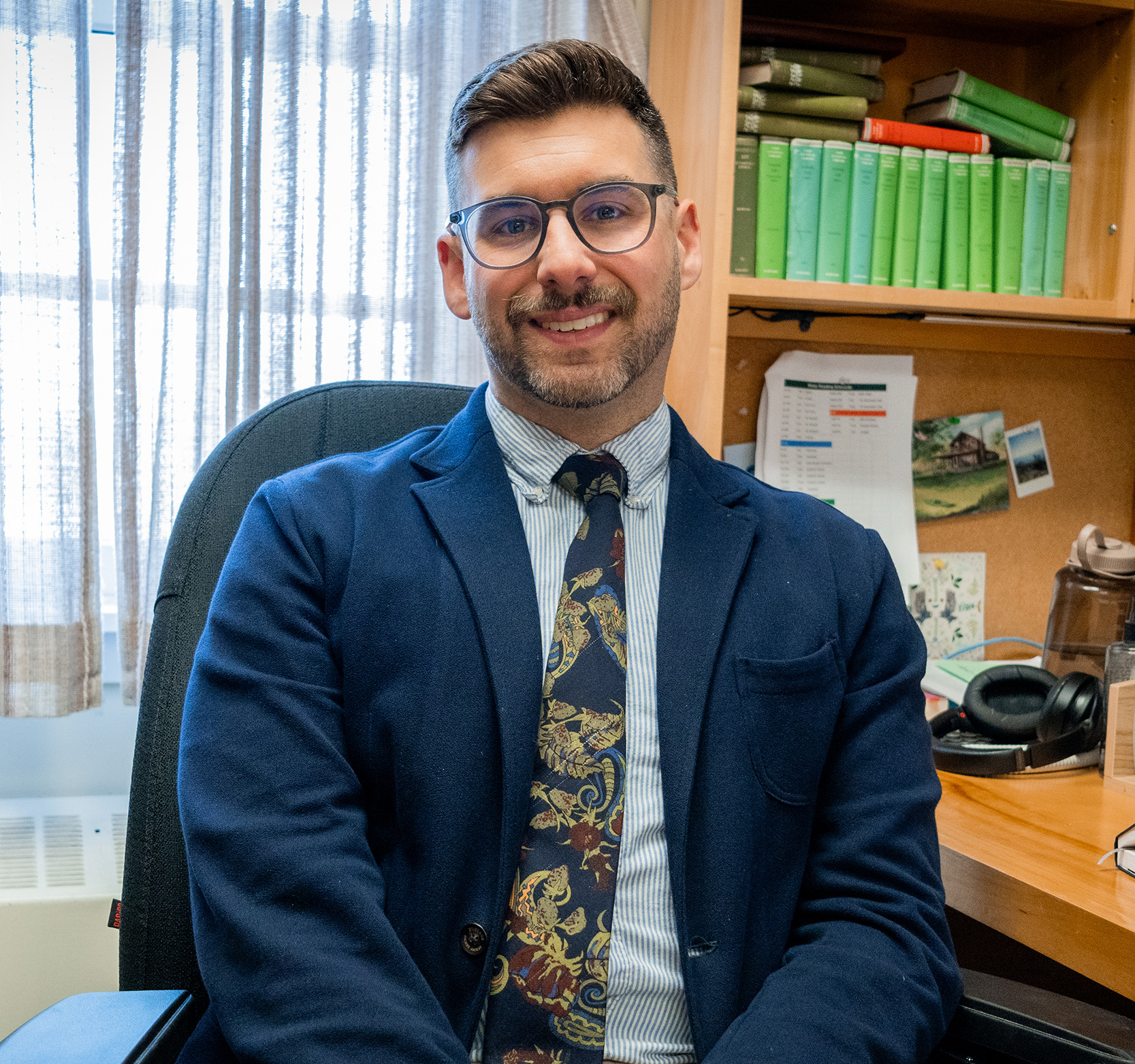 Dr. Matthew Dinan sits at his desk in front of the window
