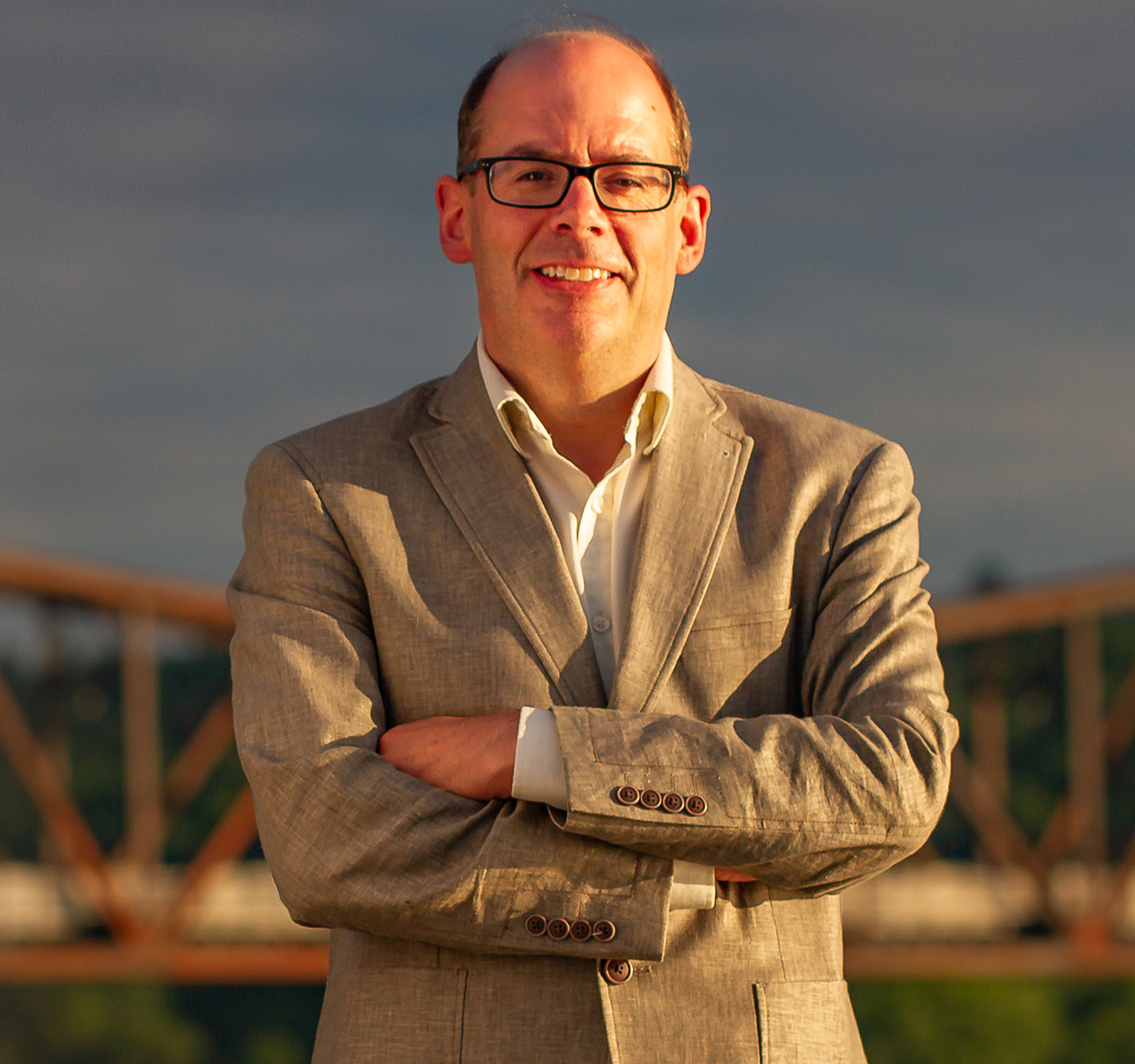 Dr. Michael Dawson standing in front of the Bill Thorpe walking bridge in Fredericton